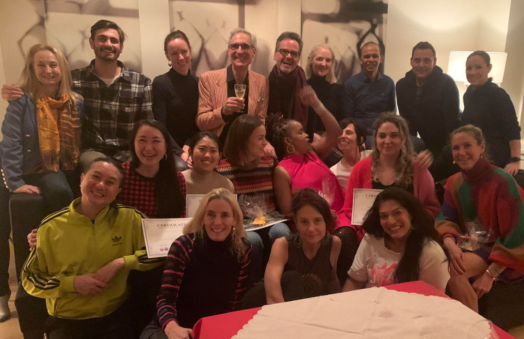 Group of people gathered indoors, smiling and celebrating with certificates and drinks, likely after a training or event.