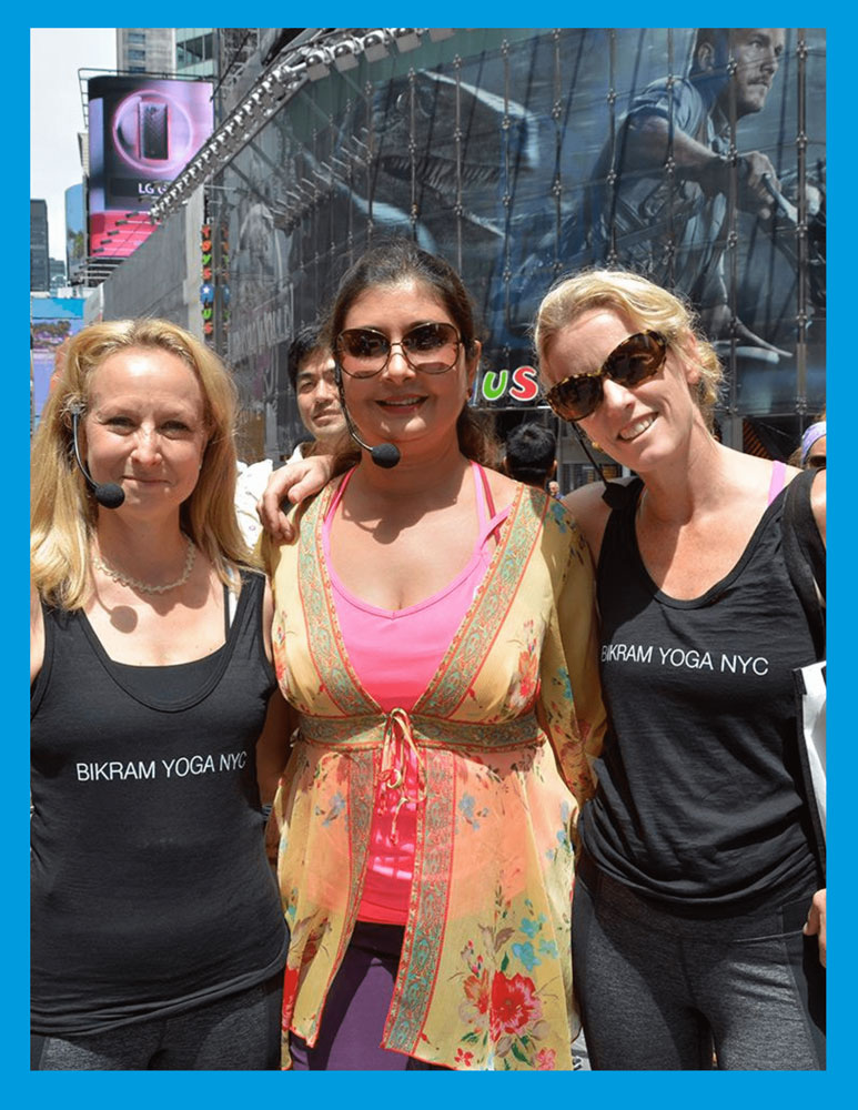 Three women smiling outdoors in NYC, wearing headsets and Bikram Yoga NYC tops, with Rajashree in the center.